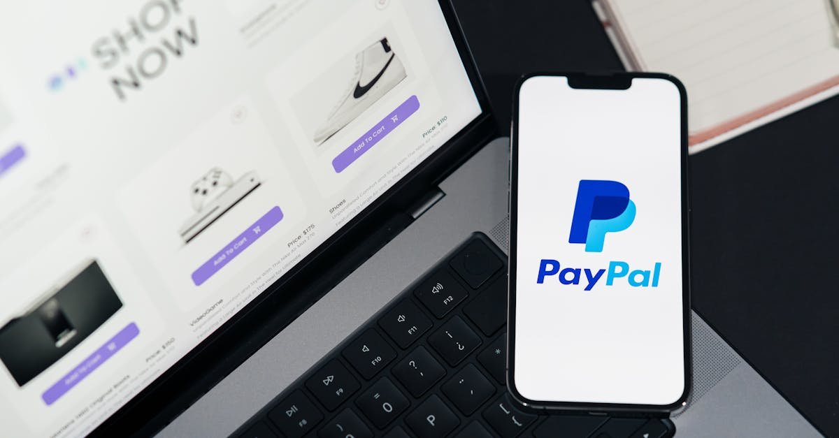 Smartphone displaying PayPal logo next to laptop with online shopping site open.